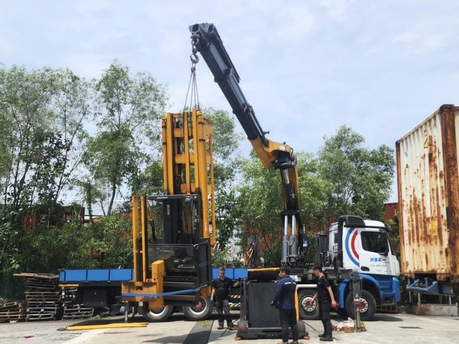 Crane lifting a forklift beside a container